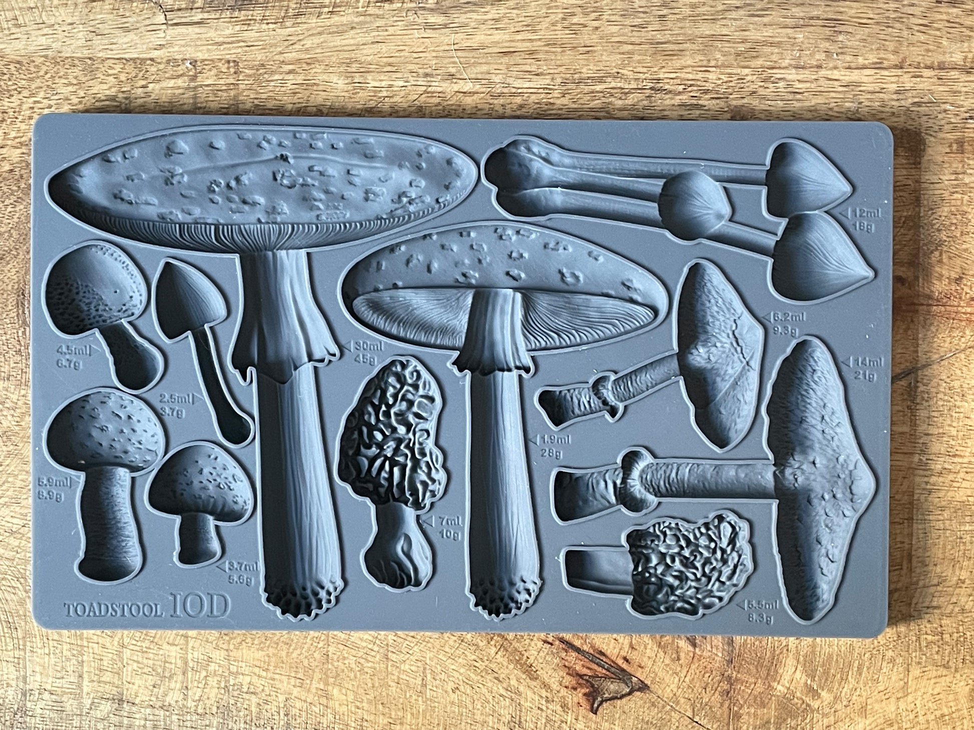 A gray-colored toadstool-shaped mold with various detailed textures, displayed on a wooden surface.