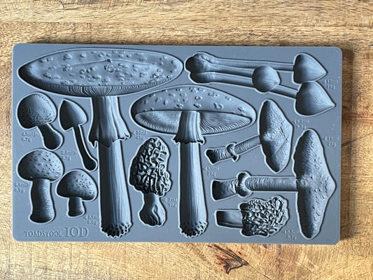 A gray-colored toadstool-shaped mold with various detailed textures, displayed on a wooden surface.