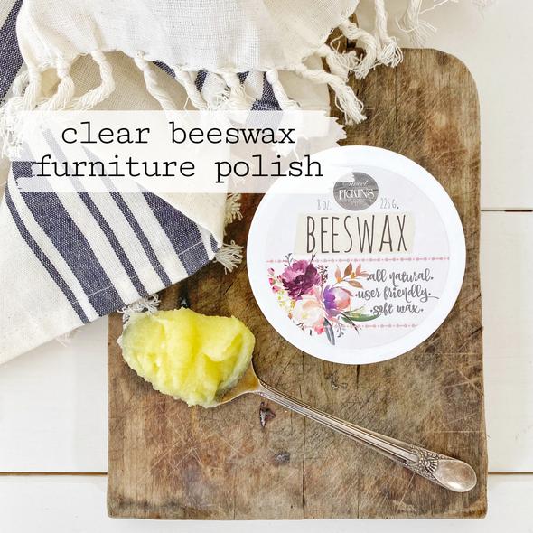 An overhead photo of beeswax jar with a spoon holding a dollop of beeswax, as well as a towel, cutting board, and the words "Clear Beeswax Furniture Polish"