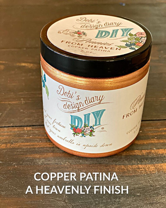 A sealed jar of Copper Patina on a wooden table with a label that reads "Debi's Design Diary, Pennies from Heaven Copper Patina".